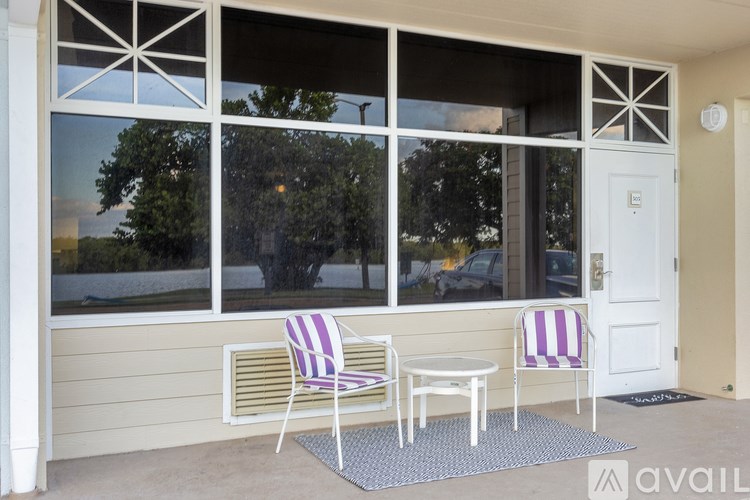 A white door is on the right side of a porch with two striped chairs and a small table.
