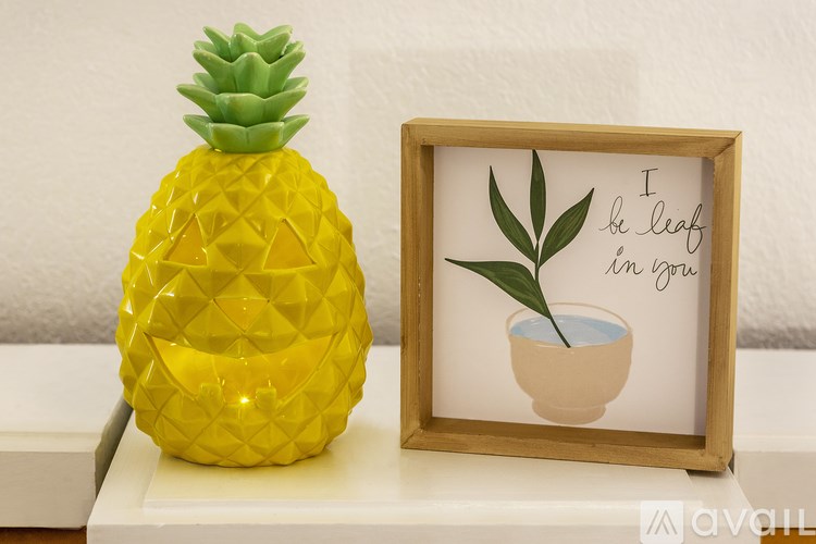 A yellow pineapple stands next to a picture of a plant in a pot.
