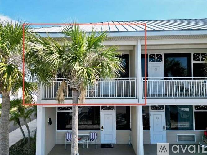 A white building with a balcony and palm trees in front.