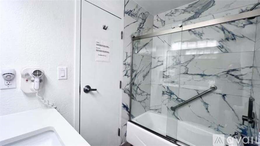 A white bathroom with a marble wall and a glass shower door.