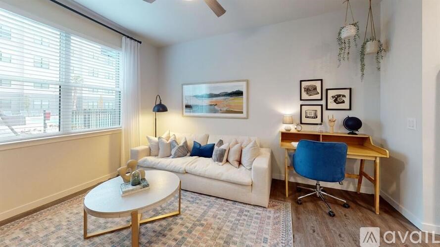 A living room with a white couch, a coffee table, a blue chair, and a painting on the wall.