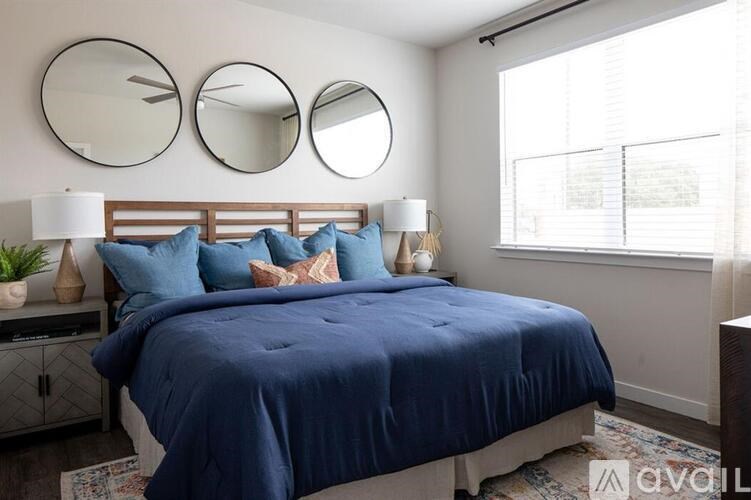 A bedroom with a blue bedspread and three round mirrors on the wall.