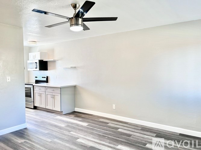 A room with a ceiling fan and a kitchenette.