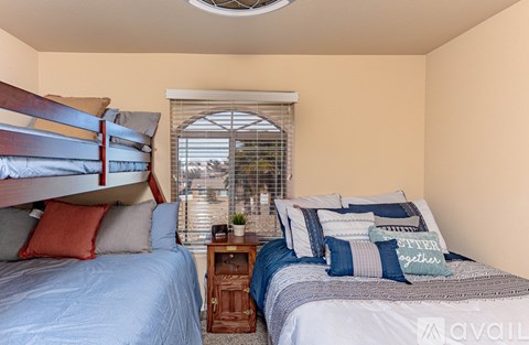 A bedroom with two beds and a window with blinds.