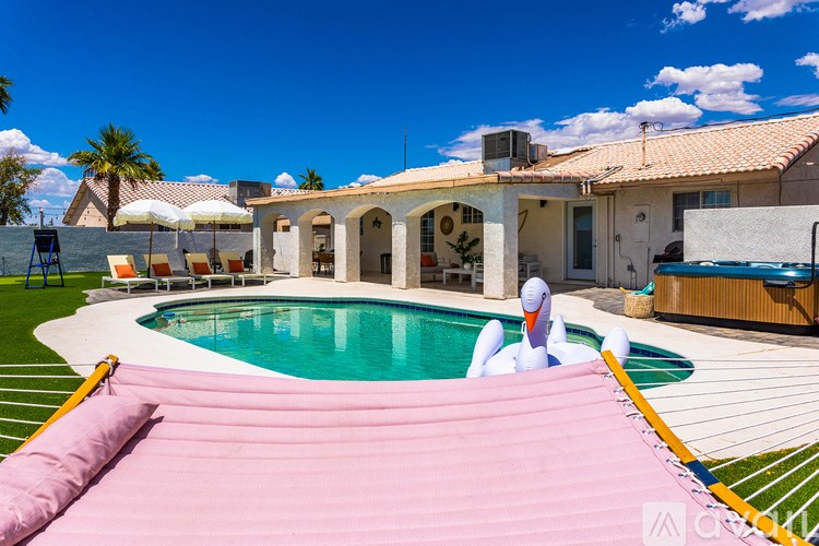 A pool with a pink cover is in the foreground of a house with a patio and pool table.