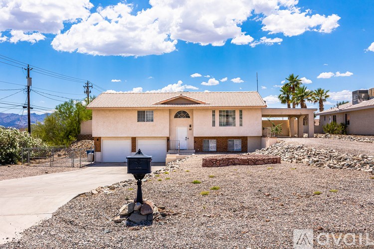A house with a brown roof and white walls is surrounded by a gravel driveway and a mailbox is in the foreground.