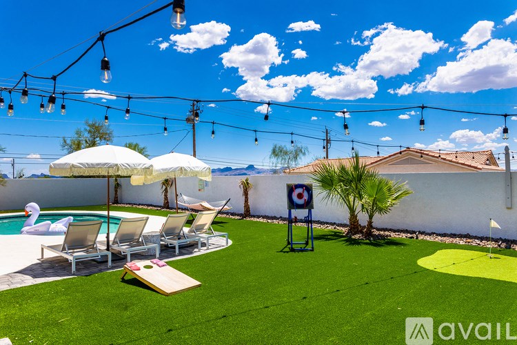 A backyard with a pool, lawn chairs, and a miniature golf course.
