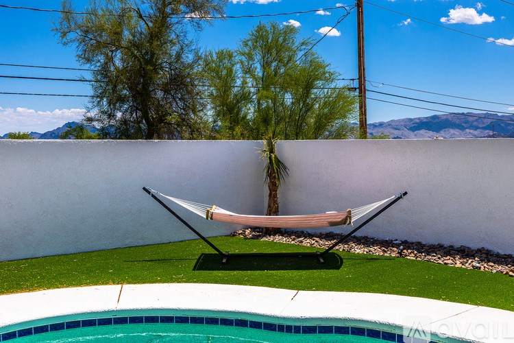 A hammock is strung between two poles on a patio next to a pool.