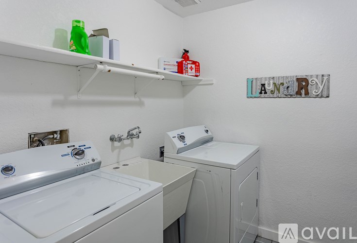 A laundry room with a washer and dryer, a sink, and a shelf with various items.