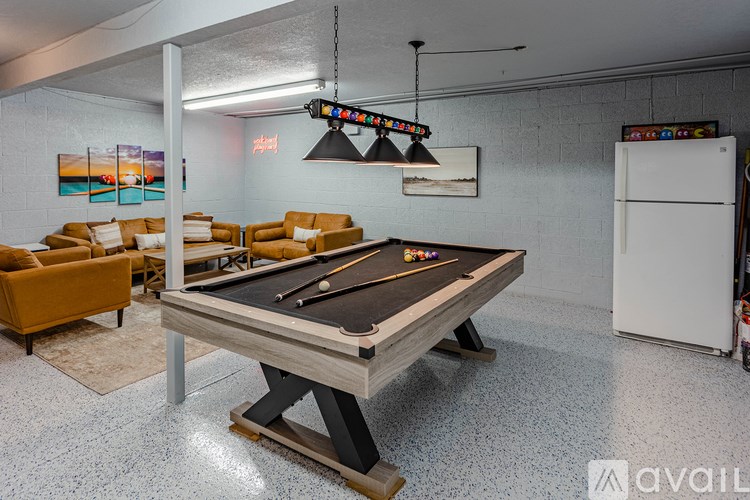 A pool table is in the middle of a room with a white fridge and a white wall.