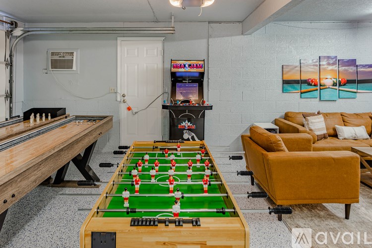 A foosball table is in the middle of a room with a pool table and a couch.