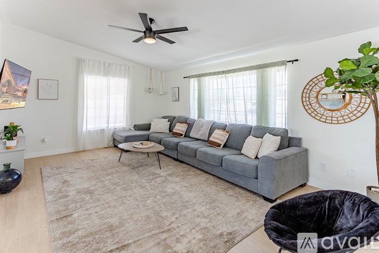 A living room with a grey couch, a rug, a ceiling fan, and a potted plant.