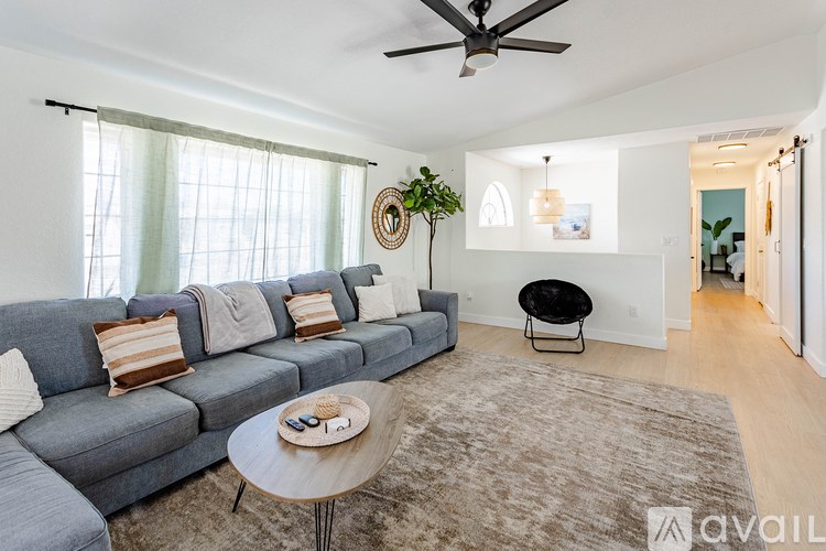 A living room with a grey couch, a round table, and a ceiling fan.