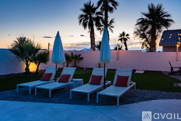 Two white chairs with red cushions are positioned under blue umbrellas.