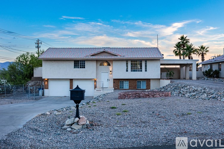 A house with a white exterior and a brown roof is surrounded by a gravel driveway and a black mailbox.