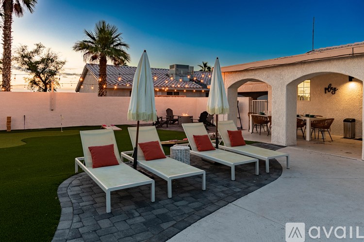 A patio with white chairs and umbrellas is set against a backdrop of a building and palm trees.