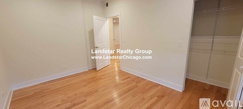 A room with wooden flooring and white walls, with a doorway leading to another room.