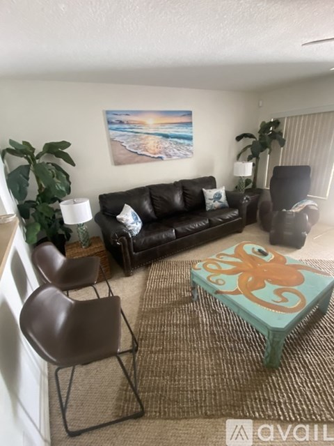 A living room with a black couch, a brown chair, a green ottoman, and a painting on the wall.