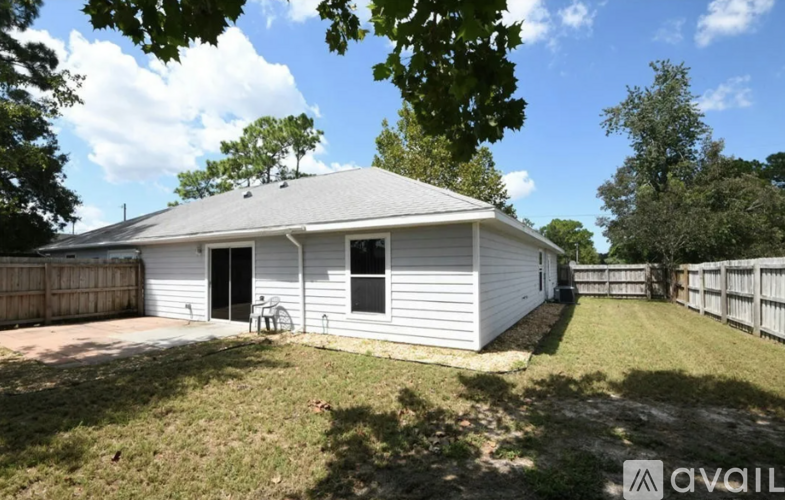A white house with a grey roof is surrounded by a fence and trees.