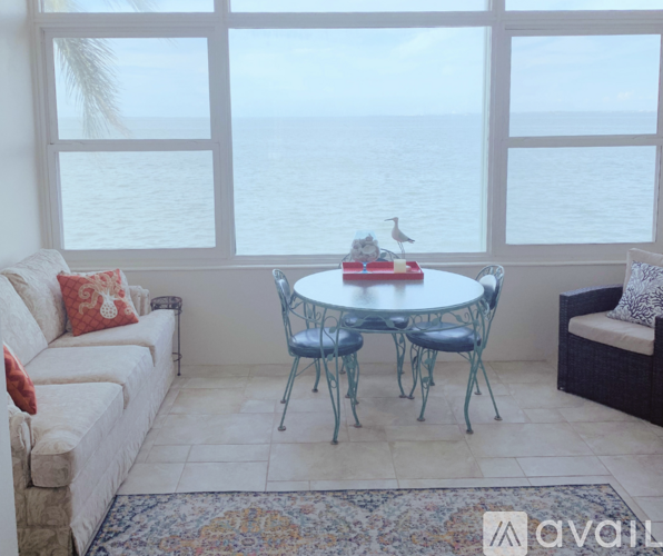 A living room with a white couch, a round glass table, and a view of the ocean through the windows.
