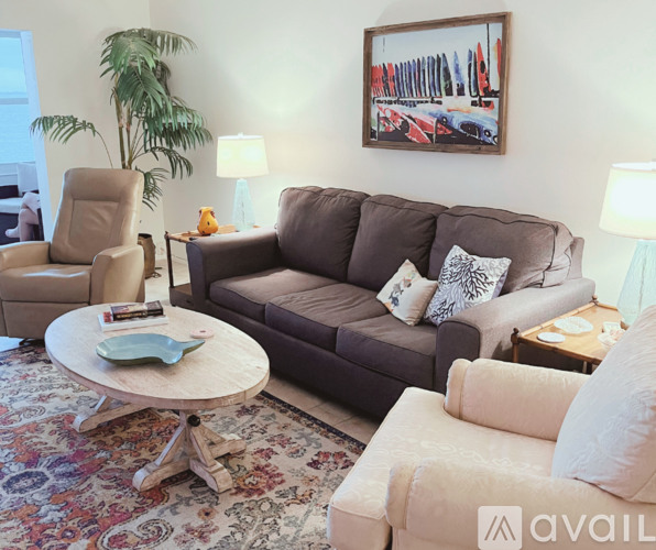 A living room with a brown couch, a chair, a coffee table, and a painting on the wall.