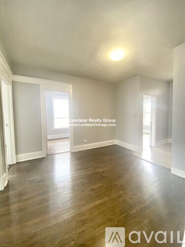 A spacious room with wooden flooring and white walls, with a window letting in natural light.