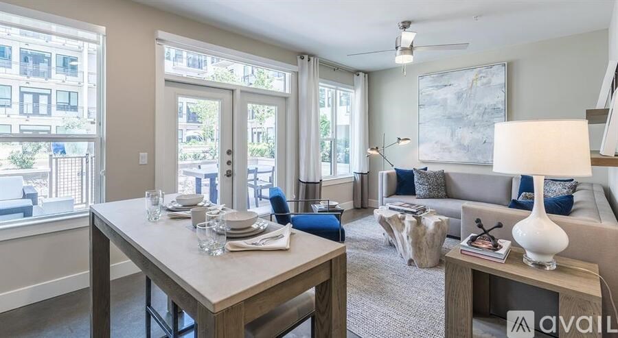 A well-lit living room with a dining table set for two and a couch with a lamp on it.