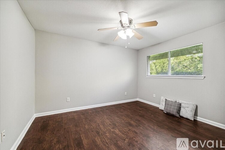 A room with a ceiling fan and a window with a view of trees.