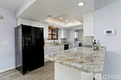 A black refrigerator is in a kitchen with granite countertops.
