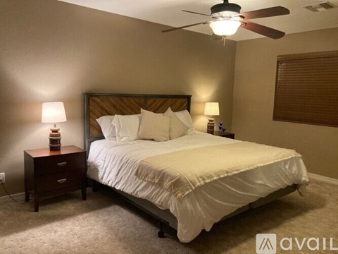 A bedroom with a bed, two lamps, and a ceiling fan.
