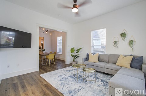 A living room with a grey couch, a yellow chair, a blue rug, and a ceiling fan.