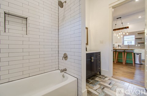 A white tiled bathroom with a tub and a wooden floor.