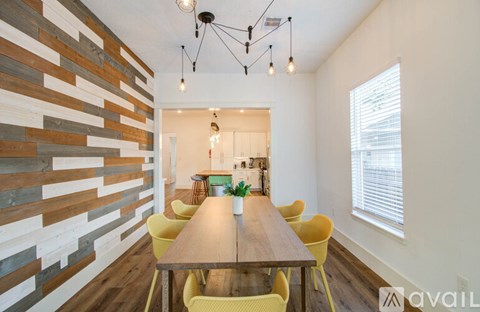 A long wooden table is surrounded by yellow chairs in a room with a wooden wall.