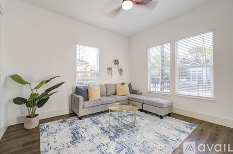 A living room with a grey couch, a blue rug, and a ceiling fan.
