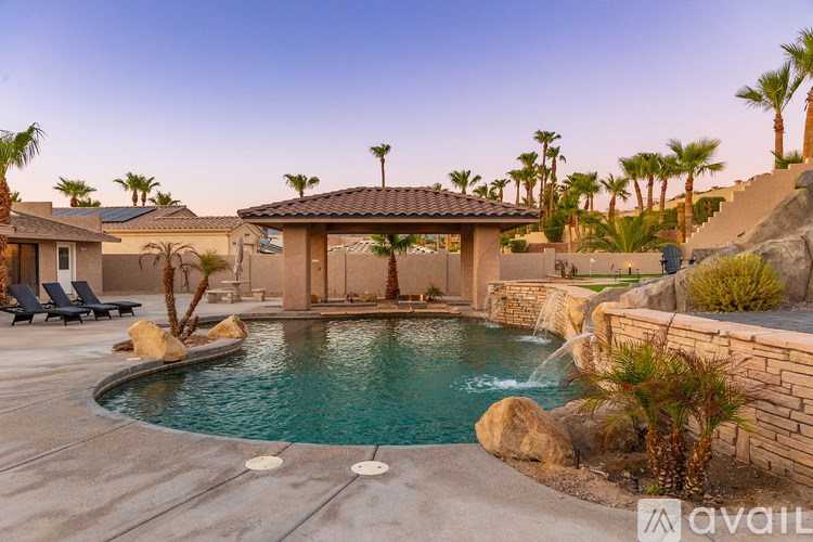 A pool with a waterfall and a gazebo in the middle of it.