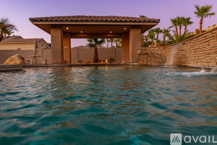 A pool with a waterfall and a gazebo-like structure in the middle.