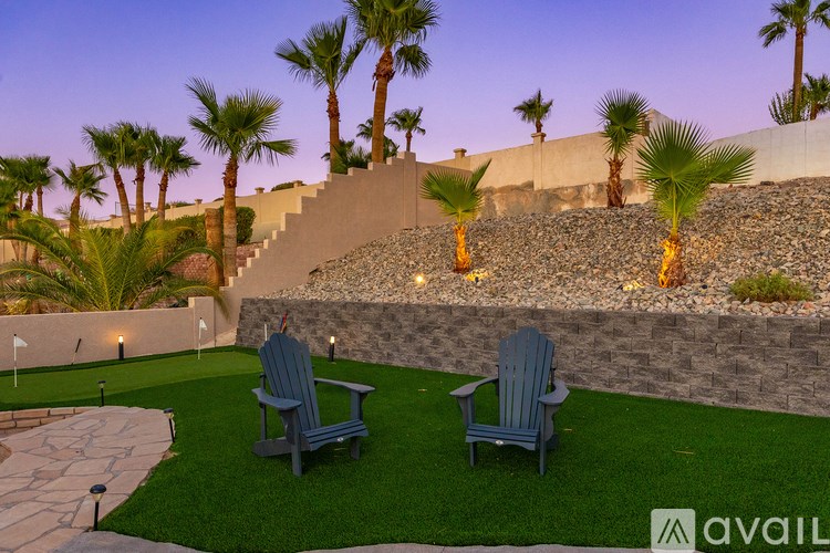 Two chairs are on a lawn with a wall and palm trees in the background.