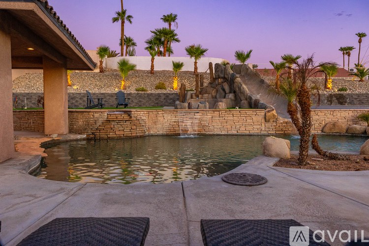 A pool surrounded by a stone wall with a palm tree and a slide.