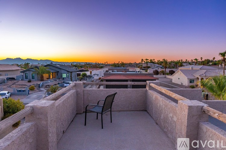 A balcony with a chair overlooking a residential area at sunset.