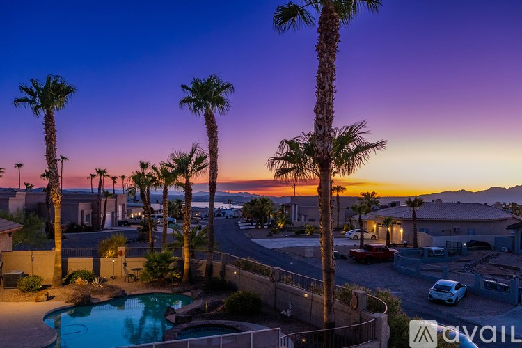 A sunset view of a pool surrounded by palm trees.