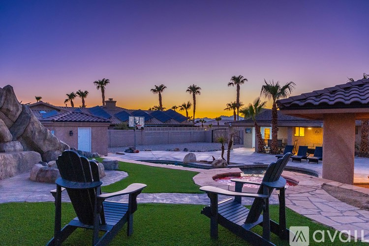 A backyard with a patio, lawn chairs, and a pool.