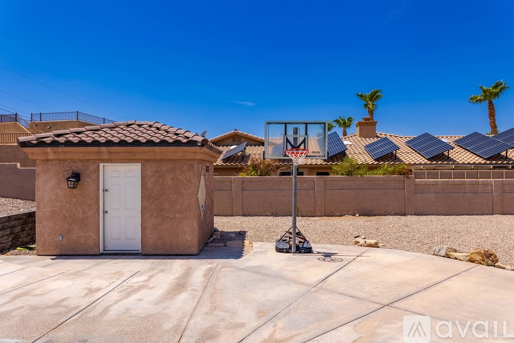 A basketball hoop is installed in a backyard with a small building and solar panels in the background.
