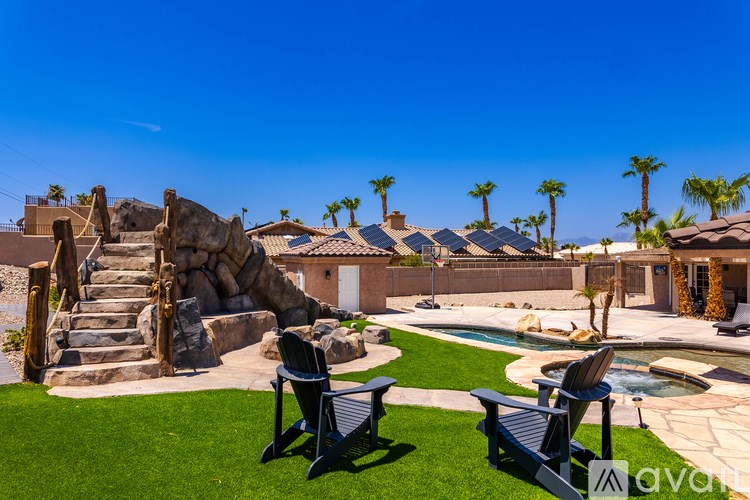 A backyard with a pool, lawn chairs, and a rock slide.
