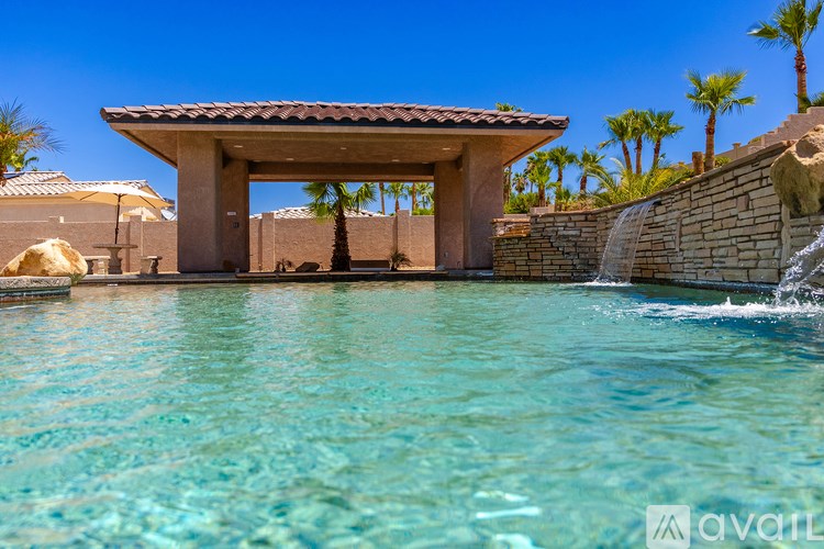 A pool with a waterfall and a gazebo-like structure in the background.
