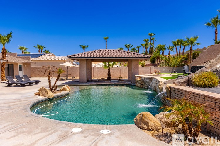 A pool with a waterfall and a patio area with chairs and a table.