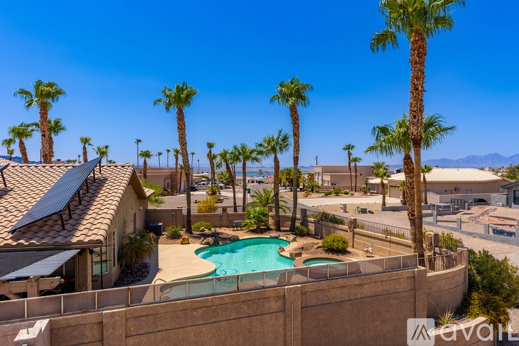 A pool surrounded by palm trees and a house with a tiled roof.