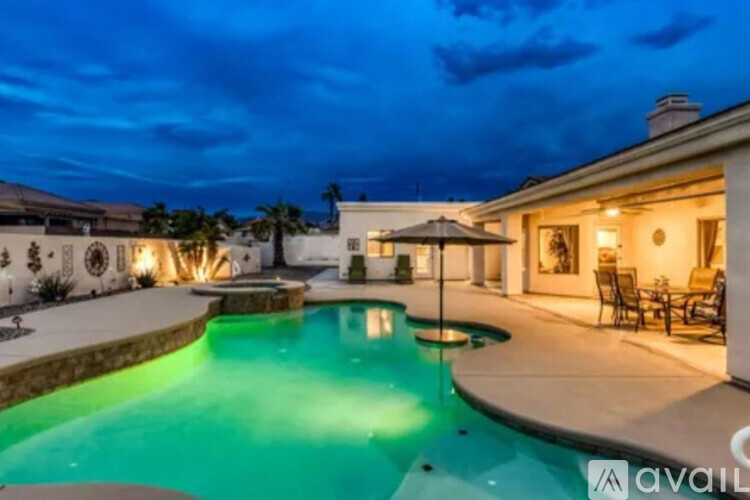 A pool with a lit up edge and a house in the background.