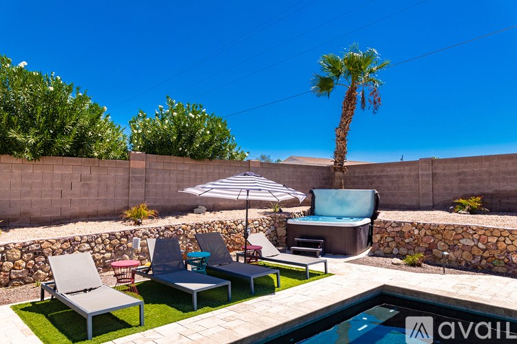 A poolside area with chairs, an umbrella, and a palm tree.