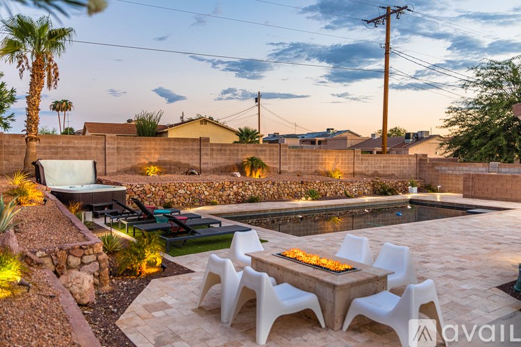 A backyard with a fire pit and white chairs.