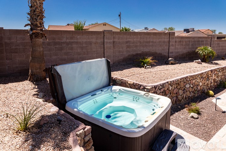 A hot tub sits in a backyard with a wall and a palm tree in the background.